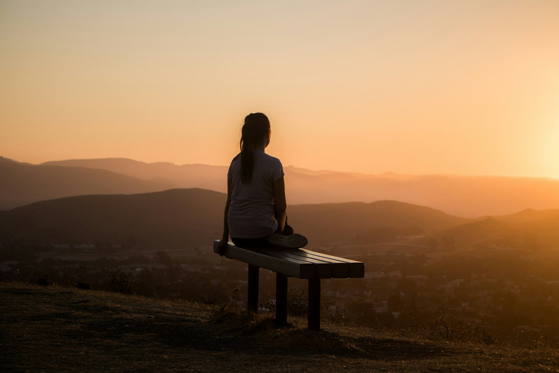 Woman sitting peacefully outdoors with eyes closed, breathing calmly — representing relief from overwhelm through hypnotherapy